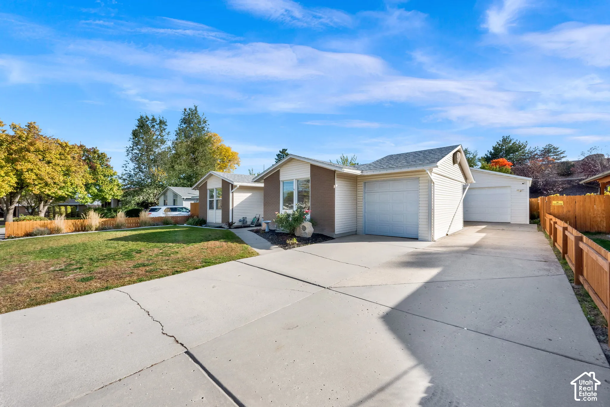 Single-story exterior featuring light-colored horizontal siding, a concrete driveway, a two-car attached garage, and wood fencing