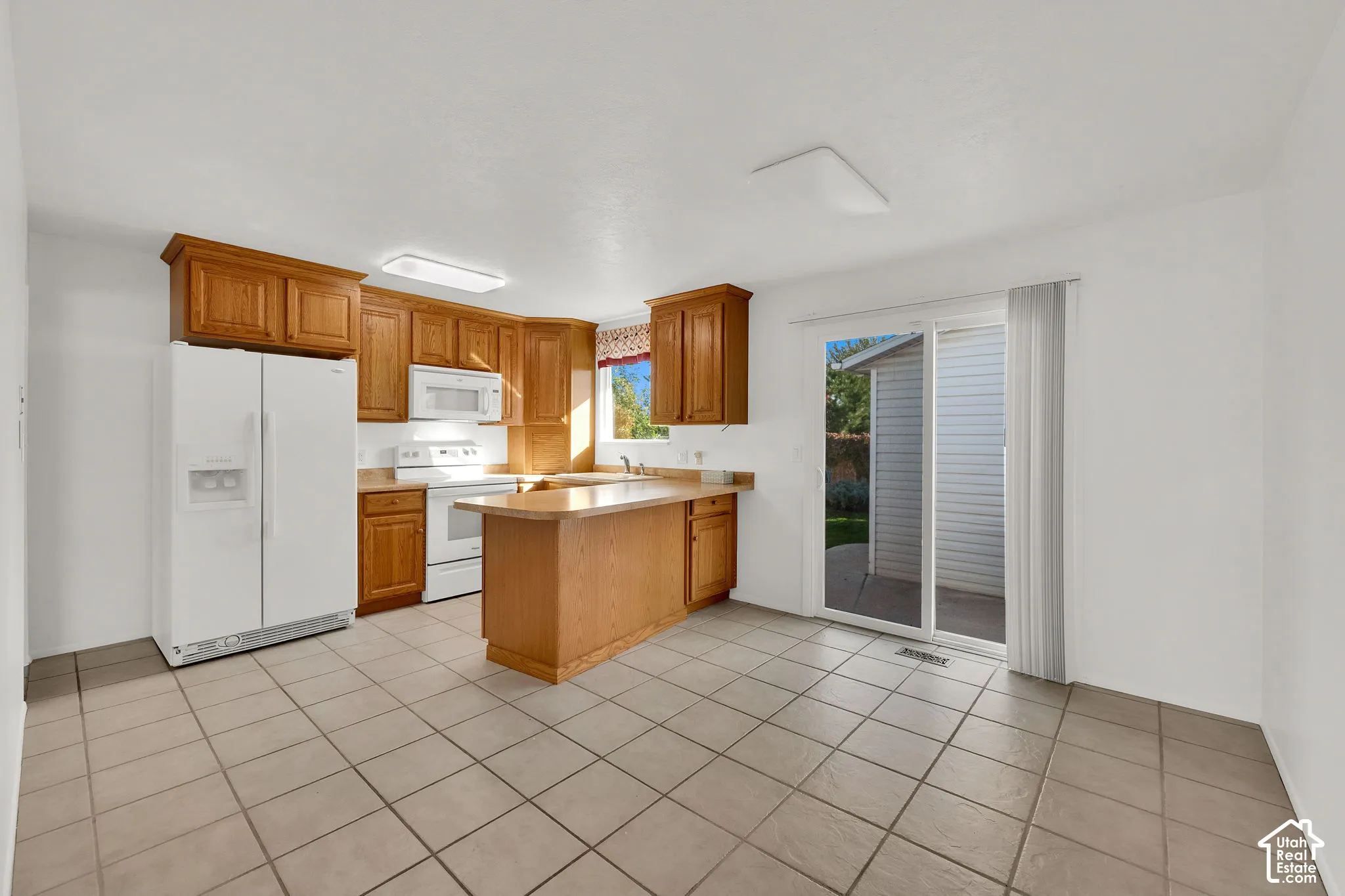 Kitchen featuring wood cabinetry, a breakfast bar, white appliances, tile flooring, and a sliding glass door