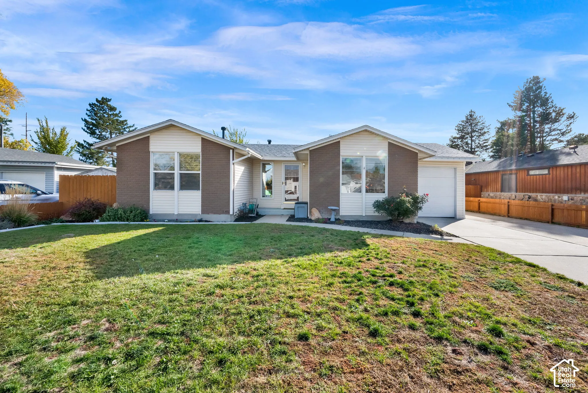 Single-story exterior featuring a brick and siding facade, an attached garage, and a front lawn with perimeter wood fencing