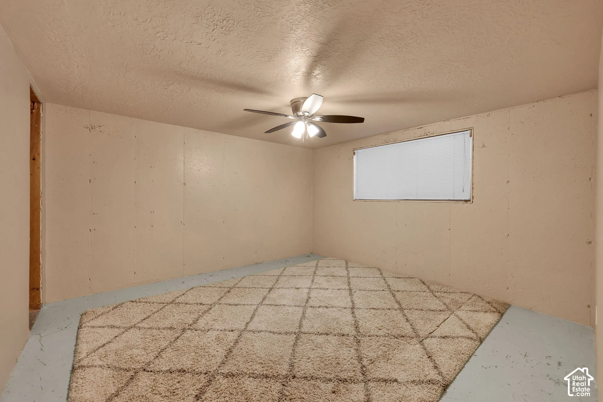 Interior space featuring textured walls, a ceiling-mounted light fixture with a fan, and a single window