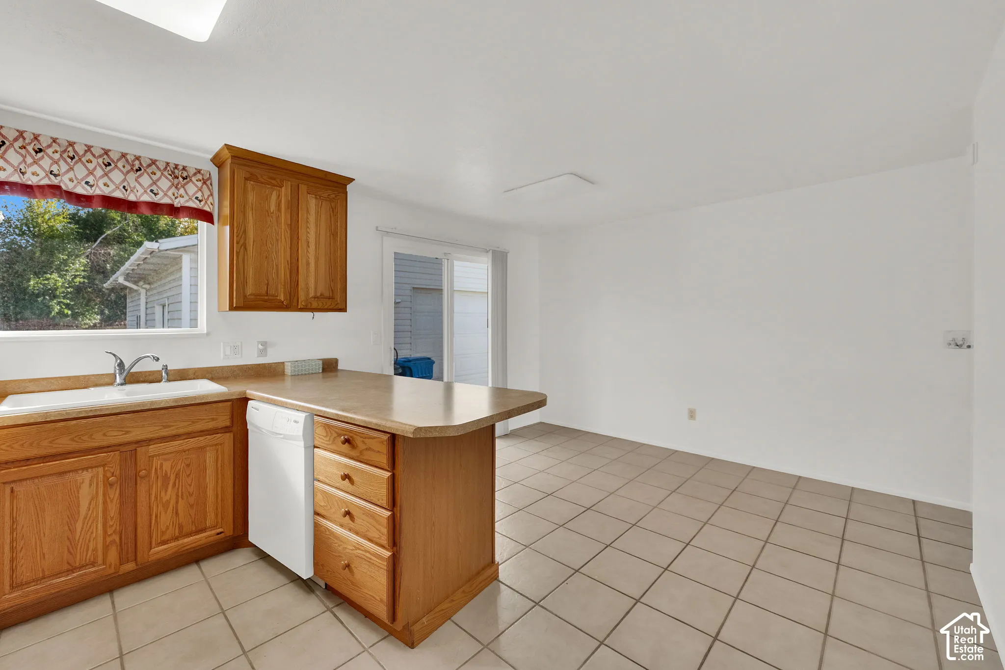 Kitchen featuring natural wood cabinetry, laminate countertops, a white dishwasher, ceramic tile flooring, and a sliding glass door