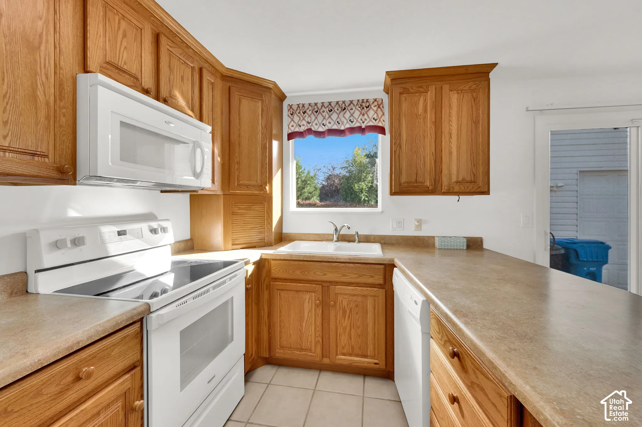 Kitchen featuring wood cabinetry, white appliance suite, dual-basin sink, laminate countertops, and ceramic tile flooring