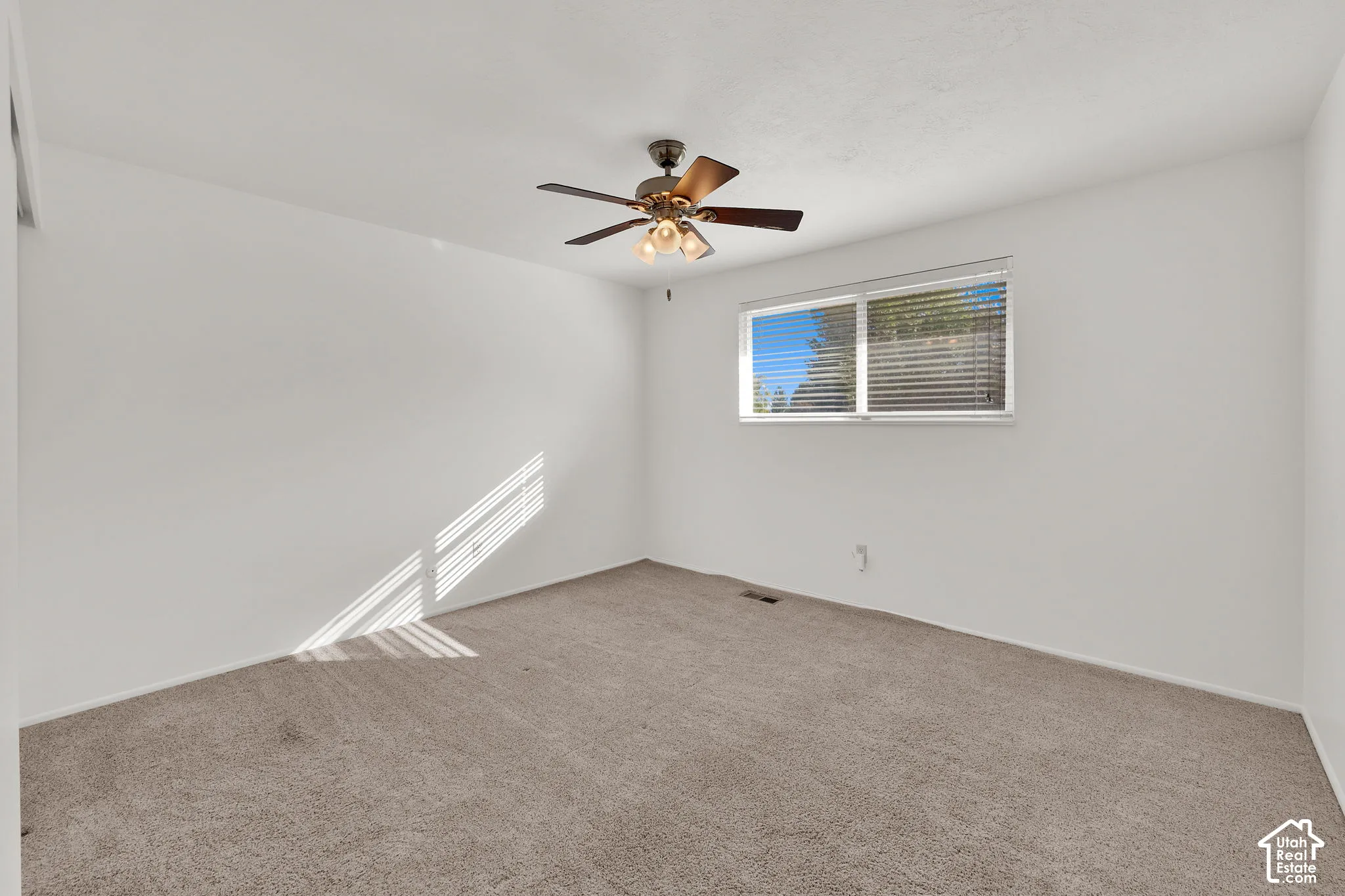 Neutral-toned carpeting, white walls, horizontal window blinds, and a ceiling fan with integrated lighting