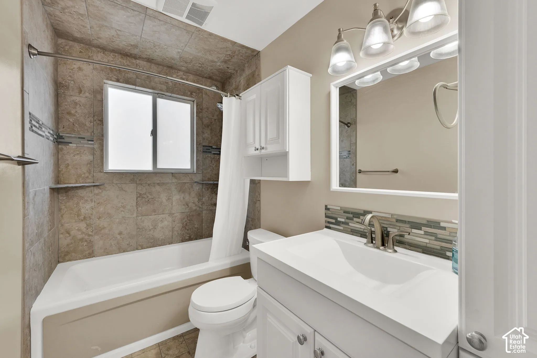 Full bathroom featuring a stone-tile tub surround with integrated shelving, white cabinetry, a rectangular sink with a metallic faucet, and a wall-mounted medicine cabinet
