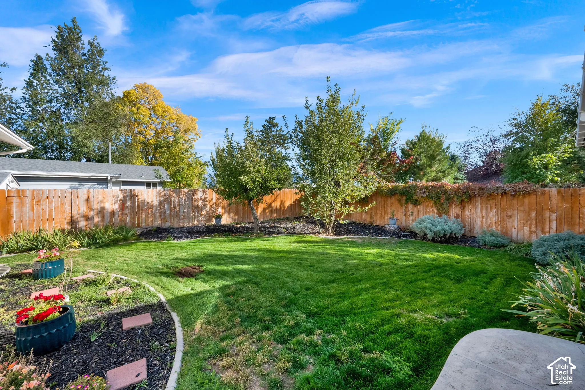 Landscaped backyard featuring a manicured lawn, perimeter wood fencing, mature trees, and defined planting beds with organic mulch