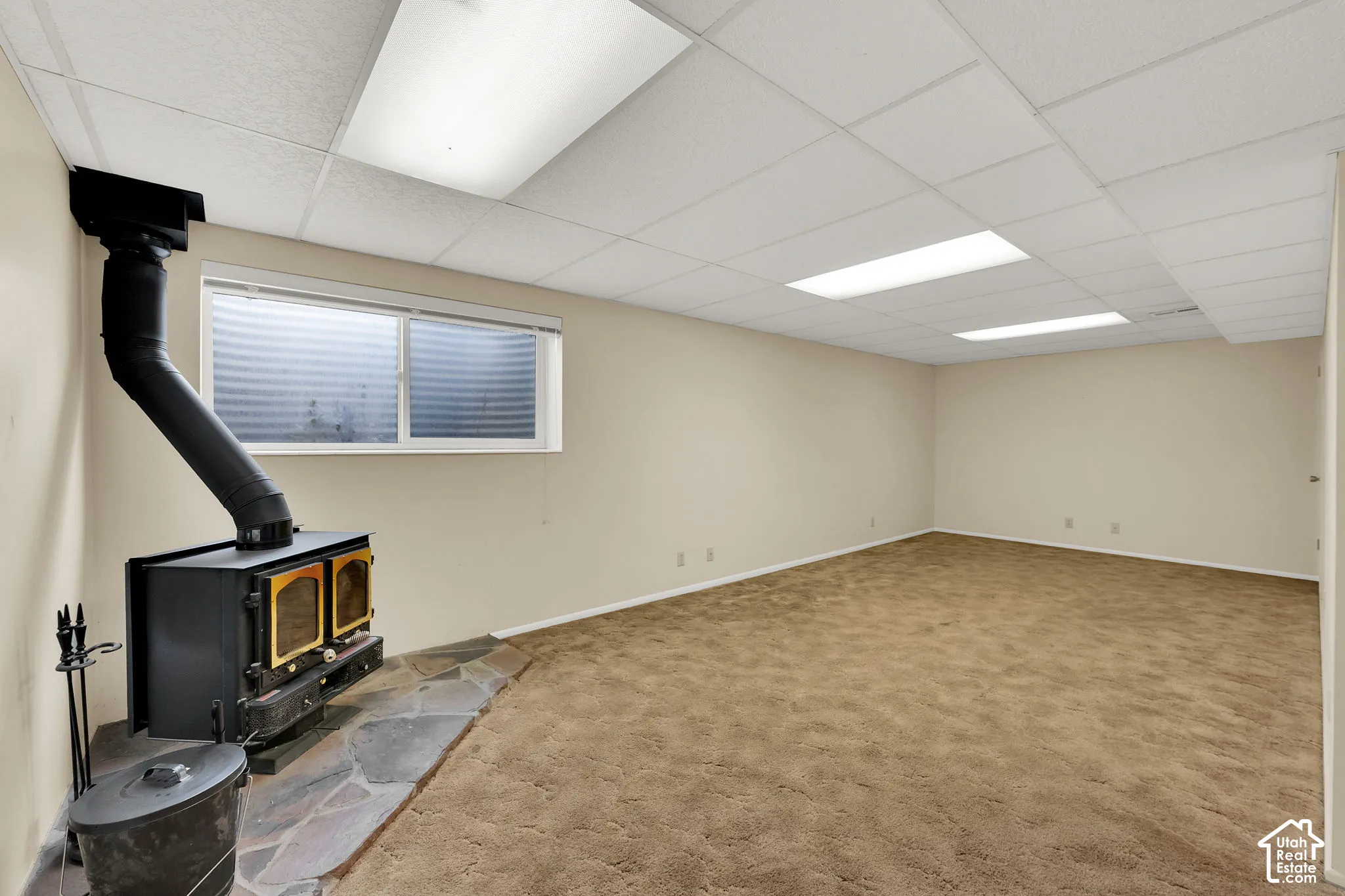 Interior space featuring a free-standing metal wood stove, stone hearth, drop ceiling with recessed lighting, and carpeting