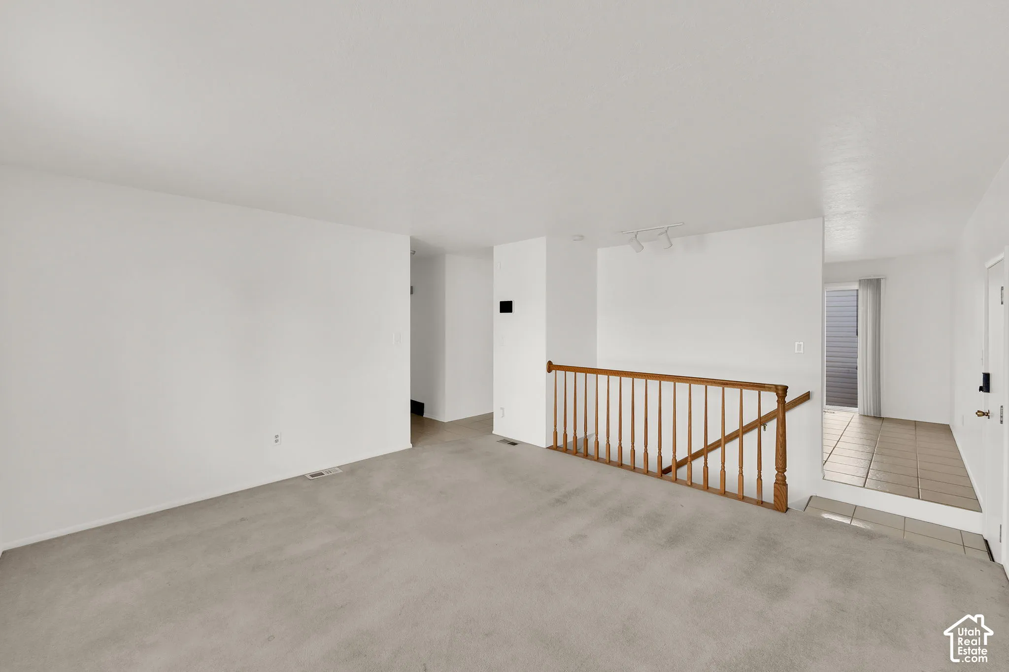 Open-concept interior featuring neutral wall-to-wall carpeting and a traditional wooden staircase railing