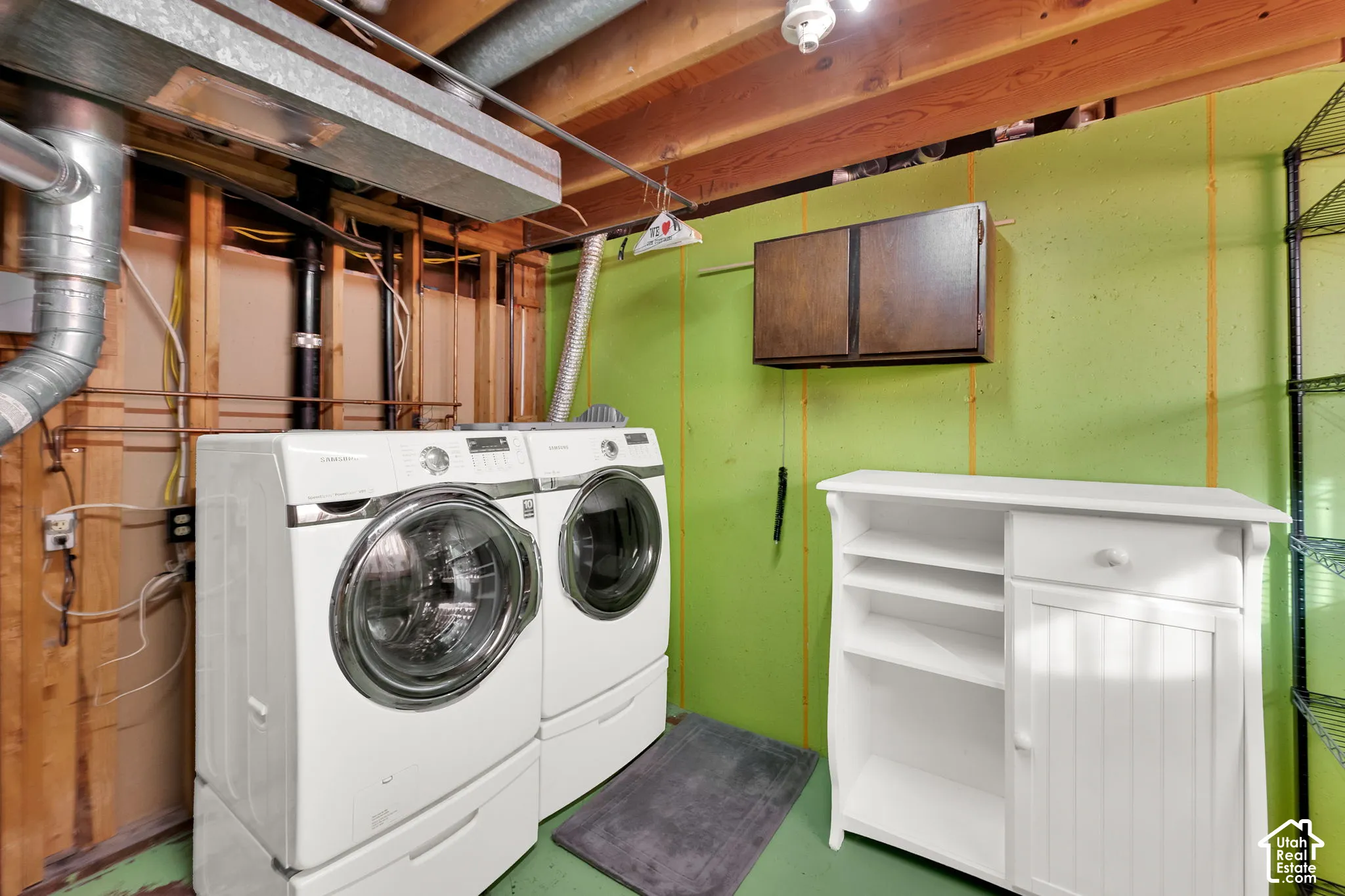 Laundry area featuring side-by-side front-load washer and dryer, wall-mounted dark wood cabinetry, and exposed joist ceiling