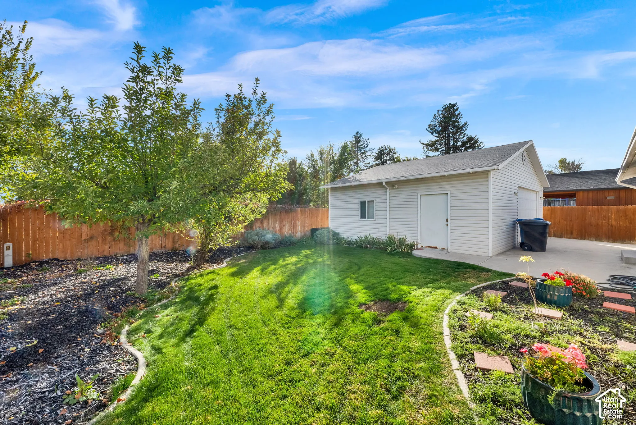Backyard featuring a grass lawn, mature trees, wood privacy fencing, concrete hardscaping, and a detached garage