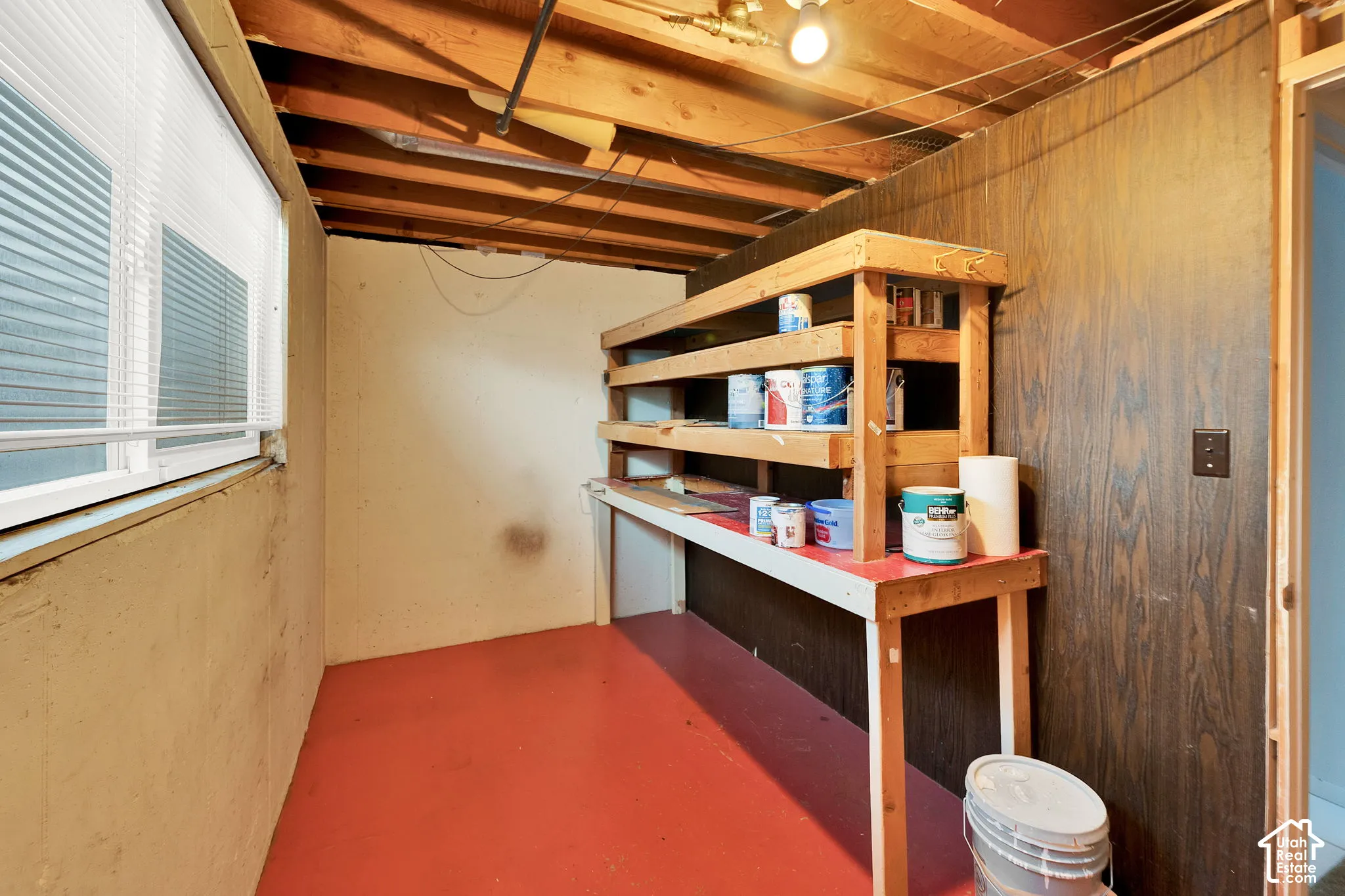 Utility space featuring a built-in wooden workbench with integrated shelving, painted concrete flooring, an exterior-facing window, and wood-paneled wall accents