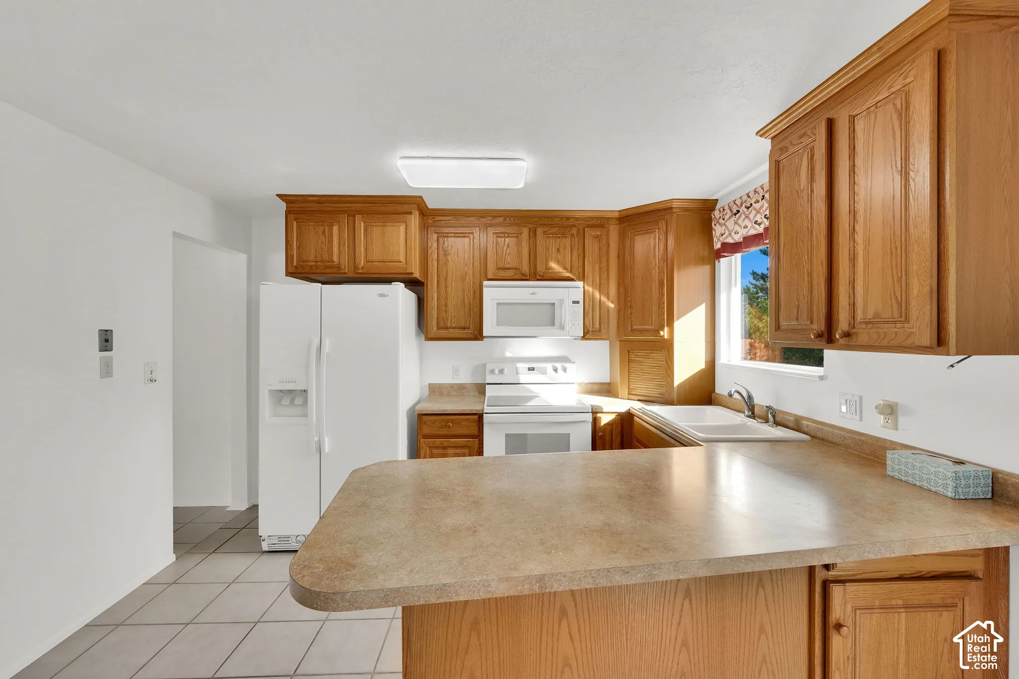Kitchen featuring wood cabinetry, laminate countertops, integrated white appliances, and tiled flooring