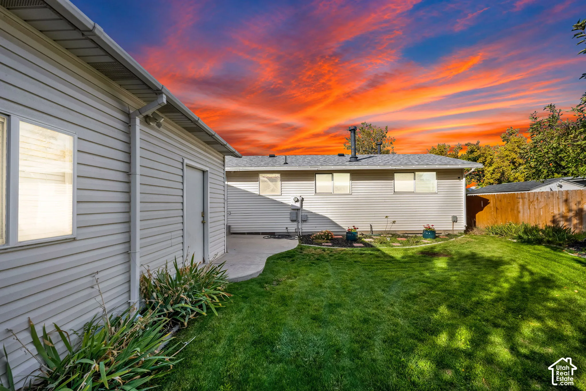 Rear exterior featuring horizontal lap siding, concrete patio, lawn area, and perimeter wood fencing