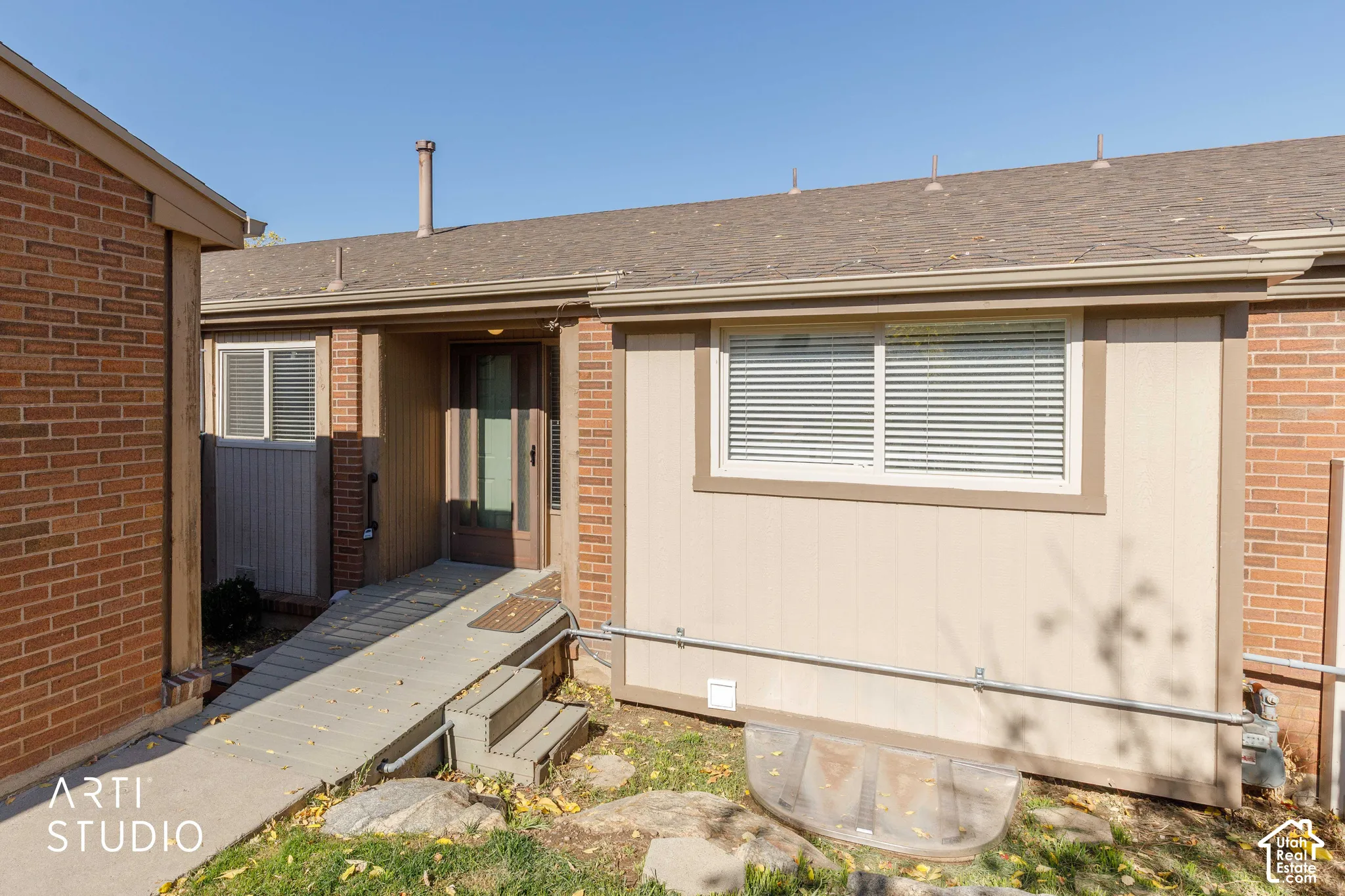 Exterior featuring brick and vertical panel siding, an asphalt shingle roof, a concrete entryway ramp with integrated steps, and a glass-panel entry door