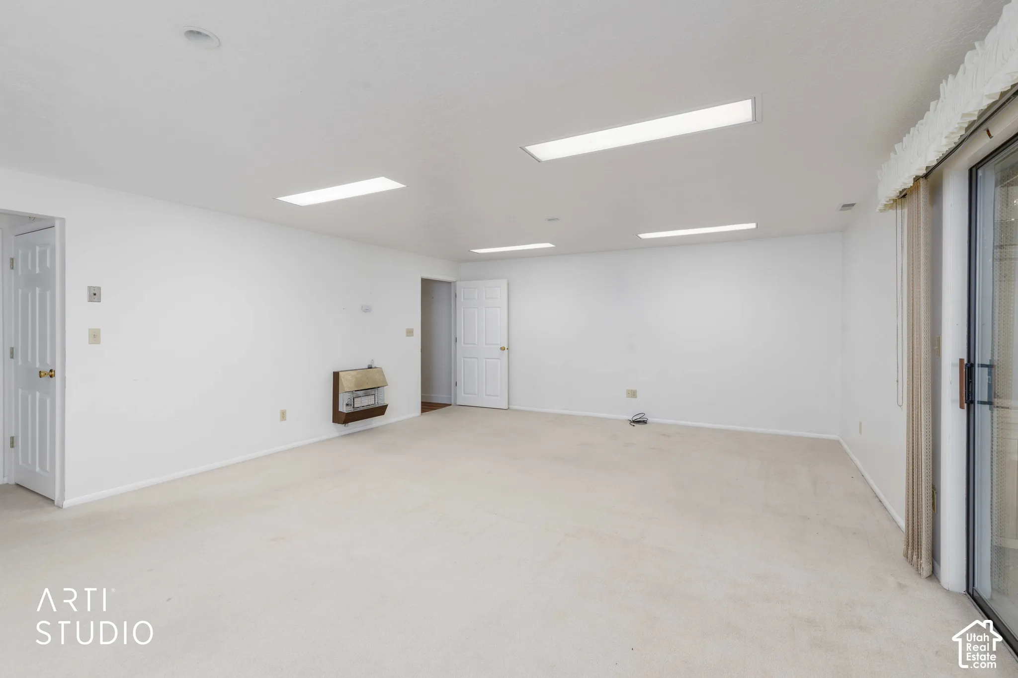 Spacious interior room featuring wall-to-wall carpeting, recessed lighting, and a wall-mounted heater unit, finished with sliding glass doors