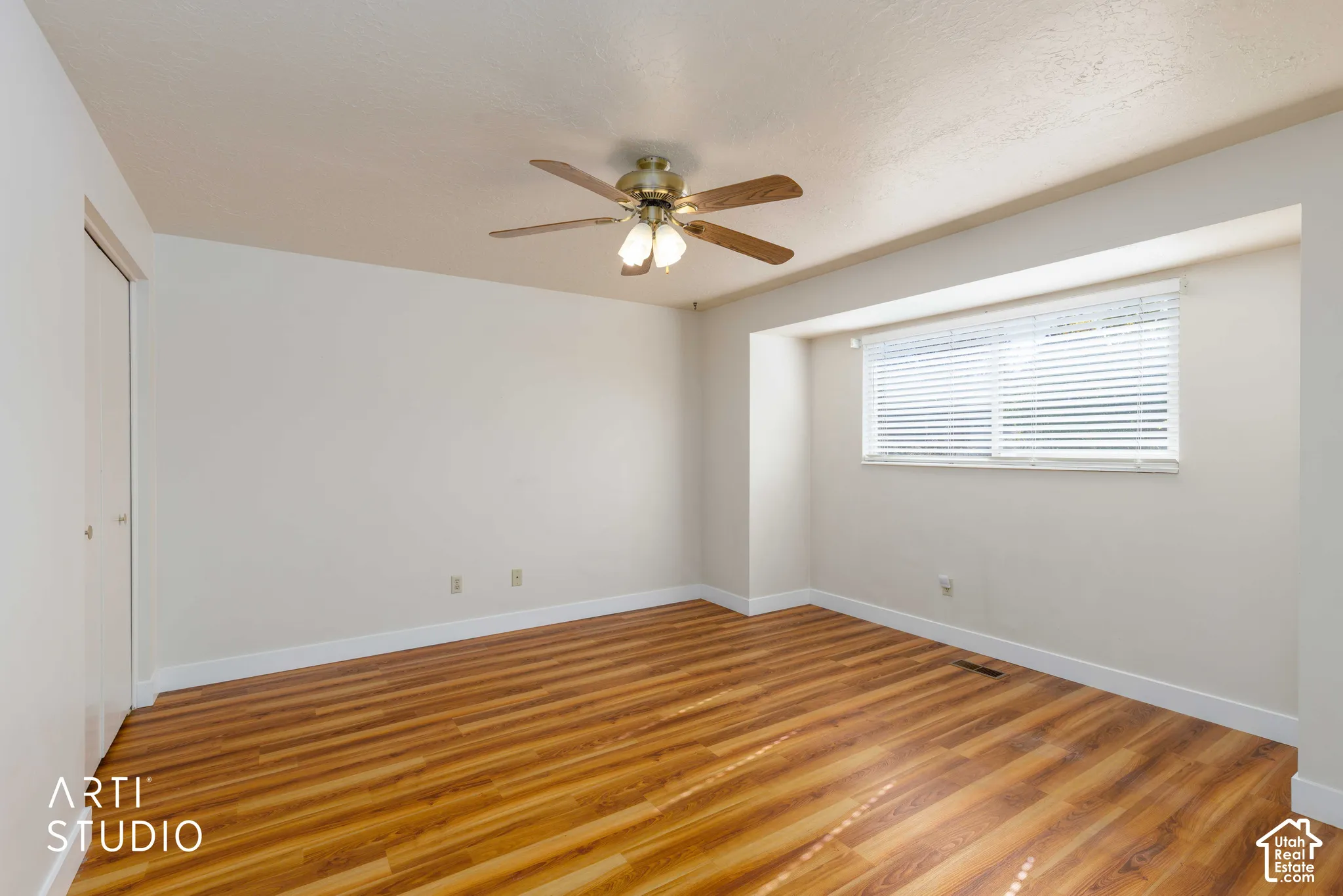 Room featuring wood-finish flooring, a recessed window alcove, ceiling-mounted fan with integrated lighting, and closet with sliding doors
