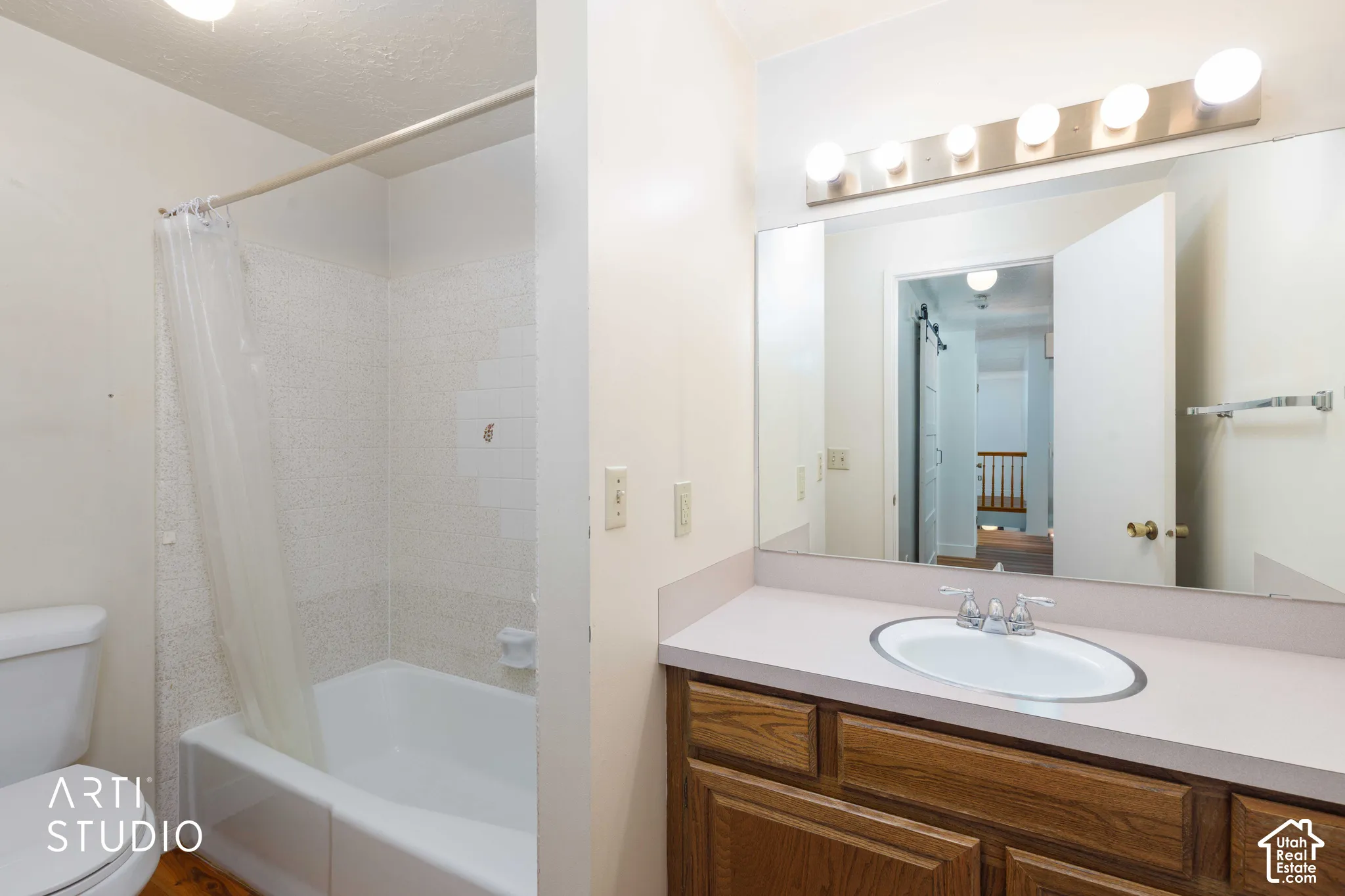 Bathroom featuring a wood-finish vanity with a solid-surface countertop, an integrated oval sink, a wall-to-wall vanity mirror, an overhead multi-light fixture, and a tile-surround tub