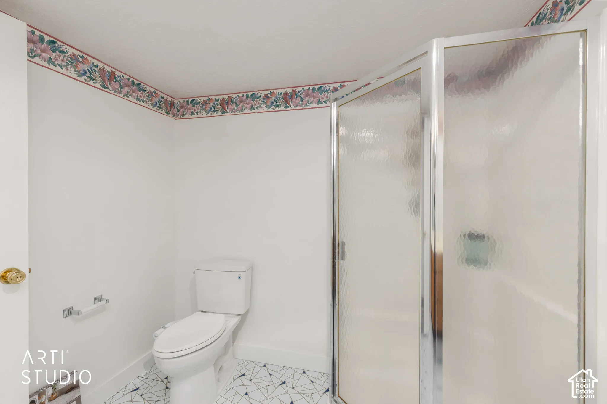Bathroom featuring a corner shower with textured glass enclosure, white porcelain toilet, and geometric patterned tile flooring
