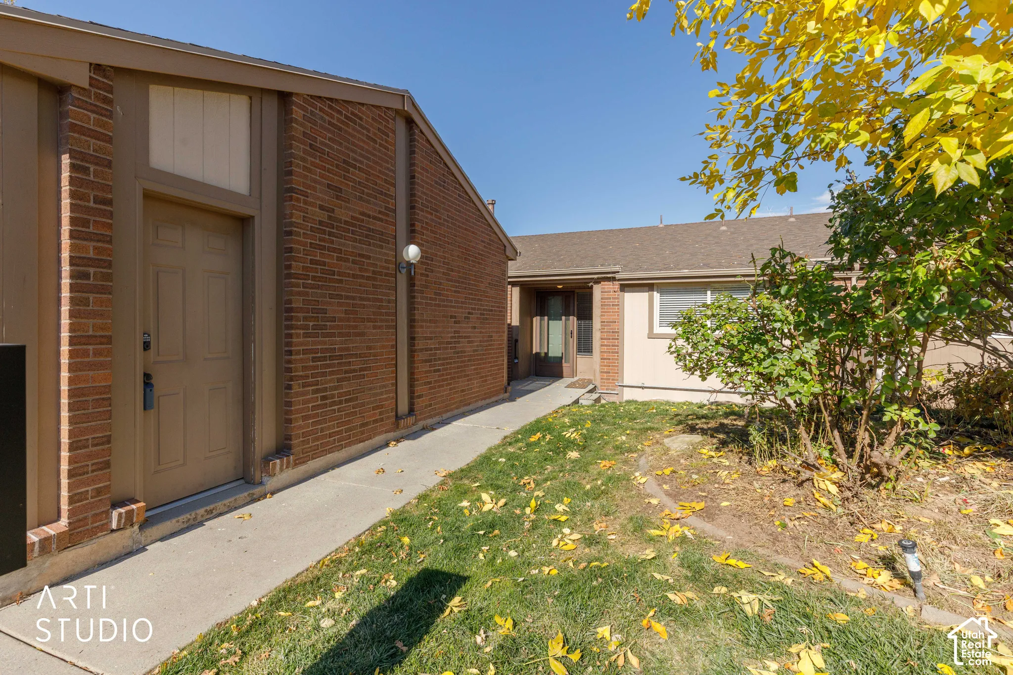 Exterior elevation featuring brown brick masonry, earth-toned siding, a concrete pathway, and an entry door with sidelight