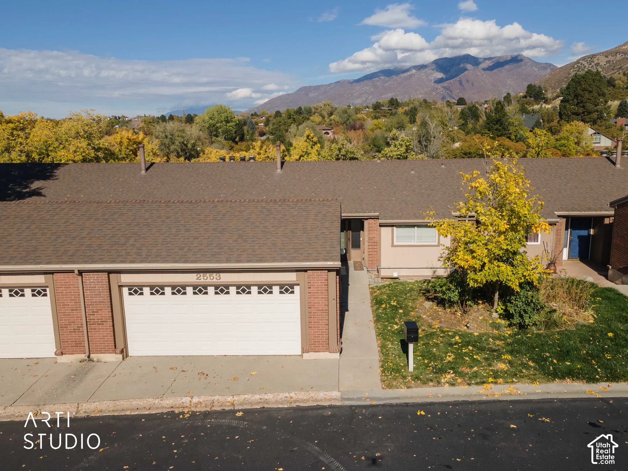 Single-story exterior featuring a brick facade, shingle roof, two-car garage, and mountain backdrop