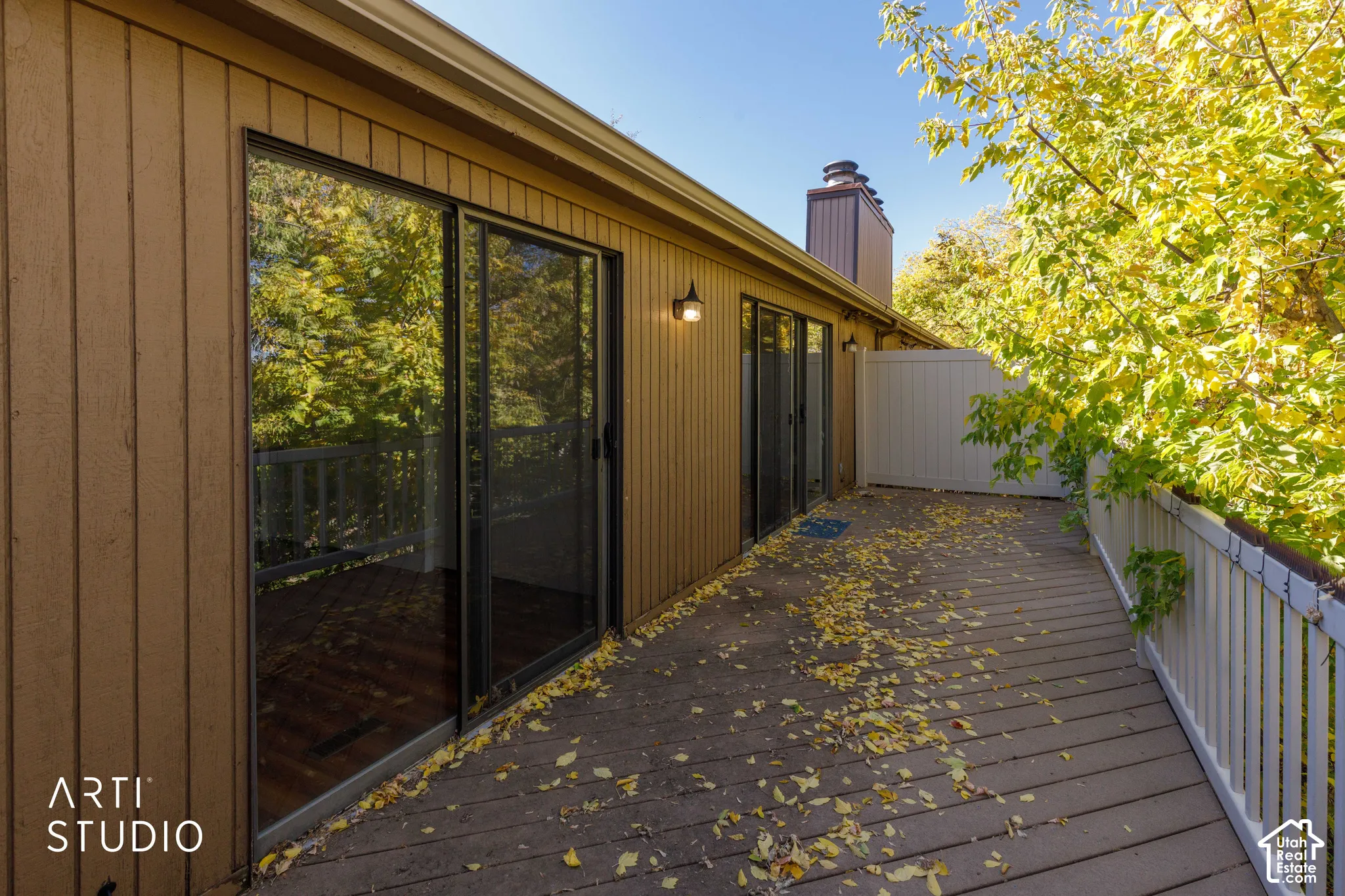 Exterior deck with vertical panel siding, multiple sliding glass doors, chimney stack, and perimeter railing