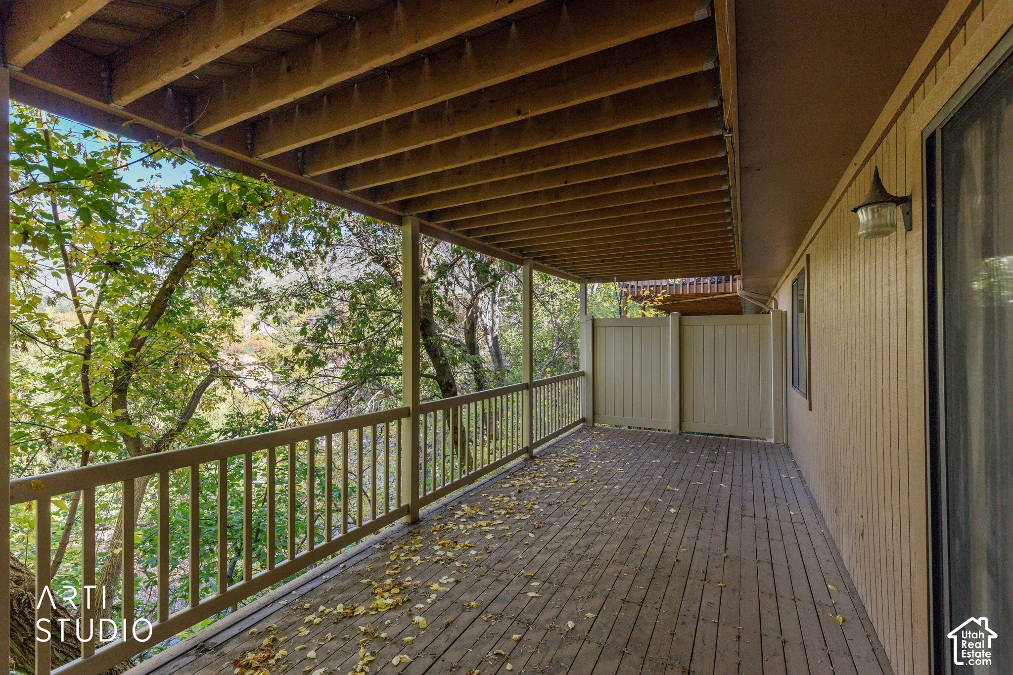Covered outdoor deck featuring a wooden balcony, vertical slat railing, and solid privacy screen