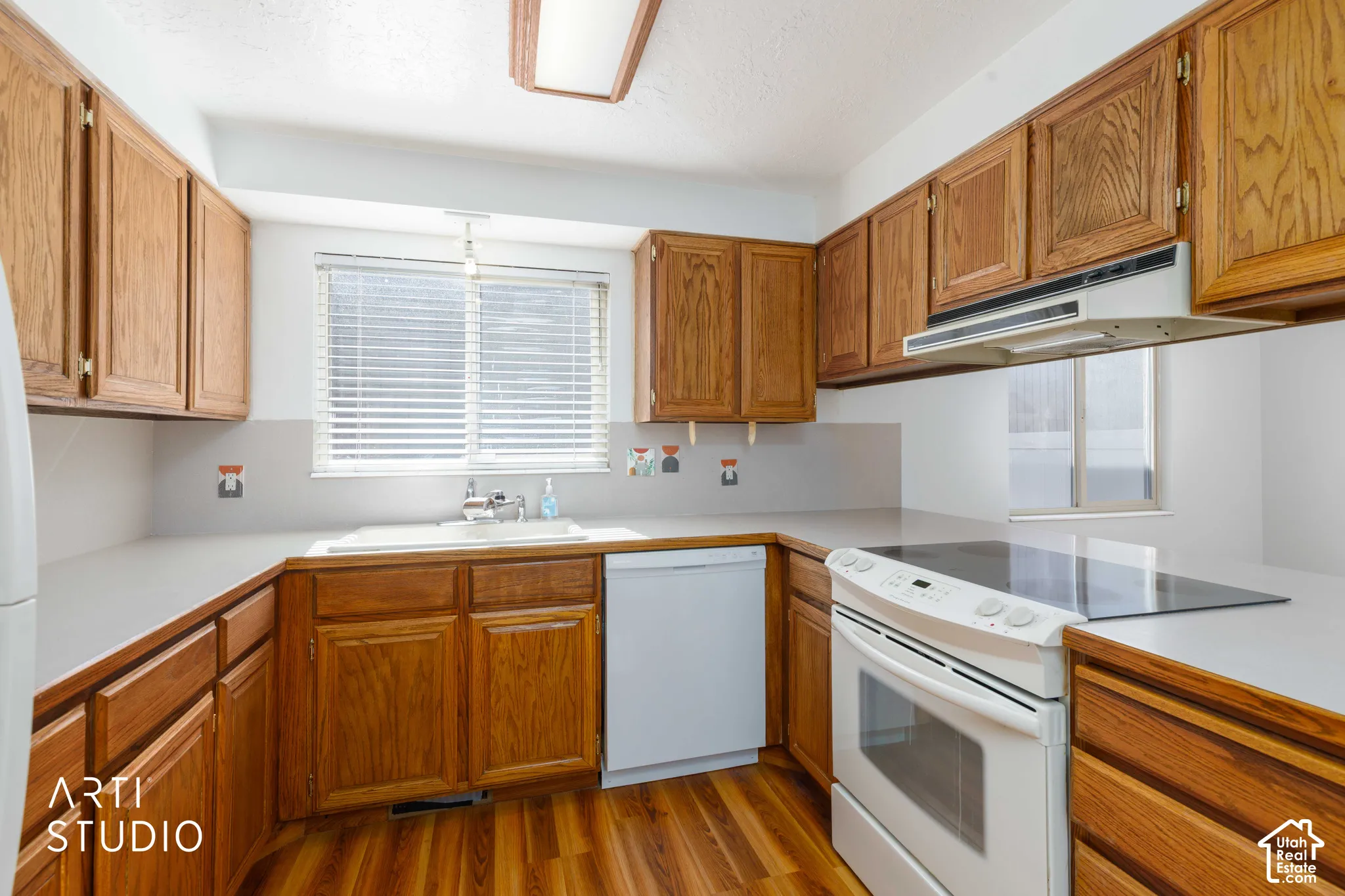 Kitchen featuring stained wood cabinetry, solid-surface countertops, wood-finish flooring, integrated electric range, and a dual-basin sink