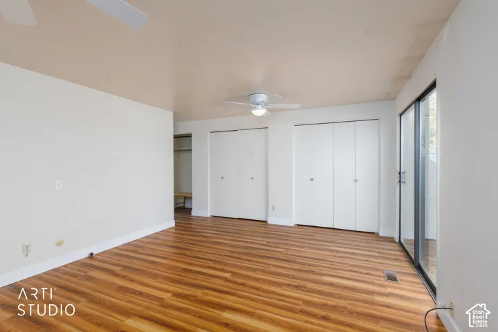 Room featuring wood-finish flooring, dual bi-fold closets, a central ceiling fan with integrated lighting, and sliding glass doors