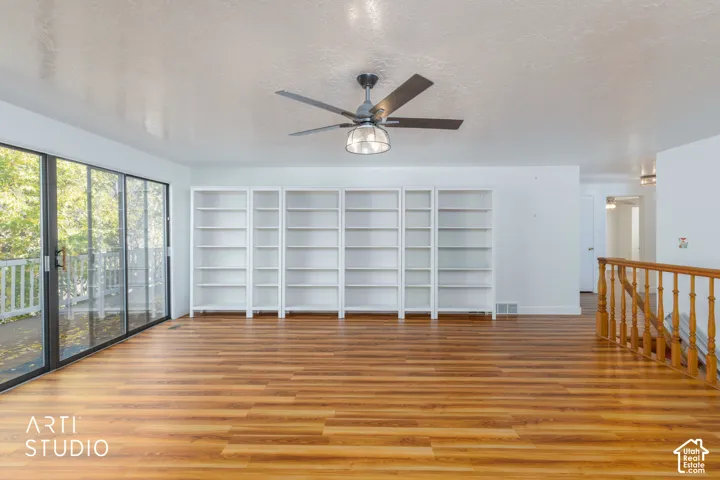 Wood-finish flooring, floor-to-ceiling built-in white shelving, sliding glass patio doors, and a ceiling fan with integrated lighting
