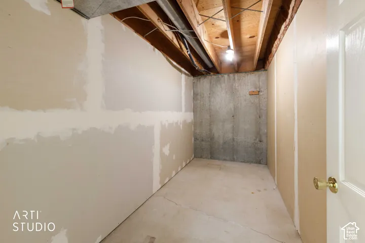 Unfinished utility room featuring drywall partition walls, concrete foundation wall, exposed wood joist ceiling, and a solid-core hinged door