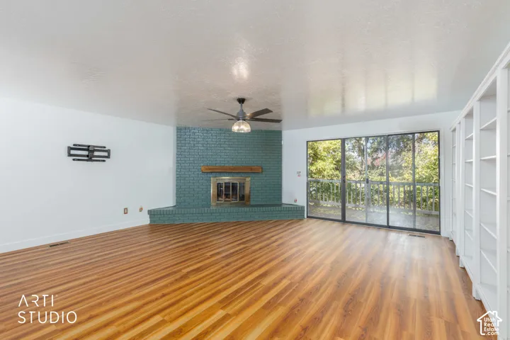 Living area featuring wood-finish flooring, a painted brick fireplace with a wood mantel, built-in shelving, a ceiling fan, and sliding glass doors
