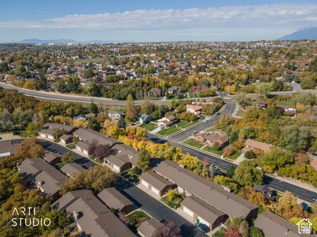 Aerial perspective featuring multi-unit structures with asphalt shingle roofing, paved driveways, and mature deciduous trees throughout the surrounding landscape