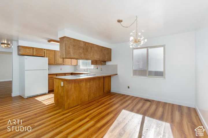 Kitchen featuring wood-finish cabinetry, a peninsula with an integrated cooktop, wood-finish flooring, and a decorative chandelier