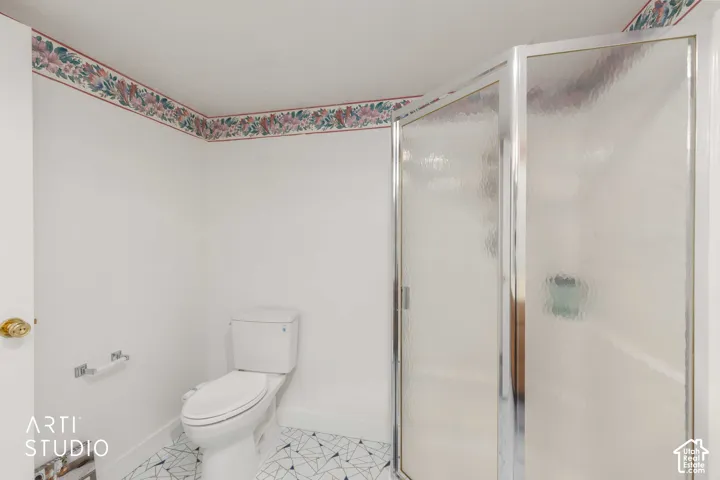 Bathroom featuring a corner shower with textured glass enclosure, white porcelain toilet, and geometric patterned tile flooring