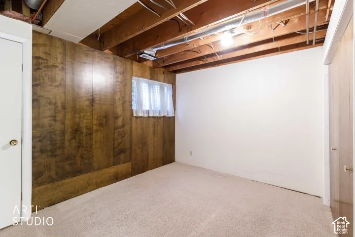 Interior space featuring wood-paneled walls, neutral carpeting, an exposed ceiling structure, and a single window