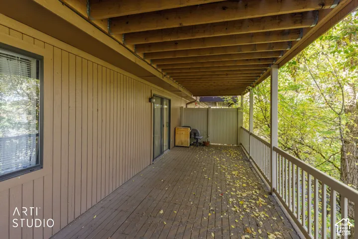 Covered wood deck featuring vertical wood siding, a wooden support beam ceiling, and a full-length painted railing