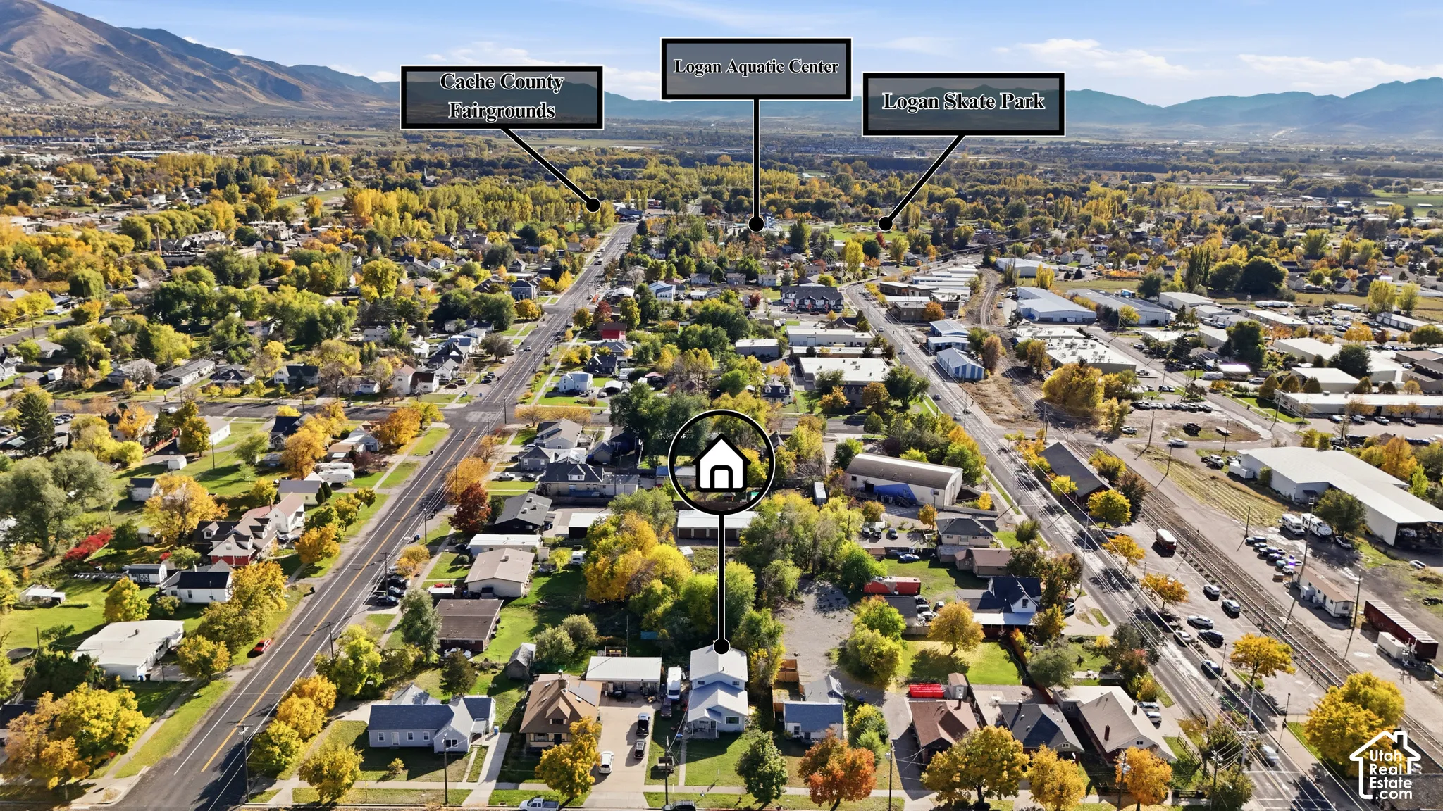 Aerial perspective of a detached residential property featuring a paved driveway, mature trees, and a mountain range backdrop