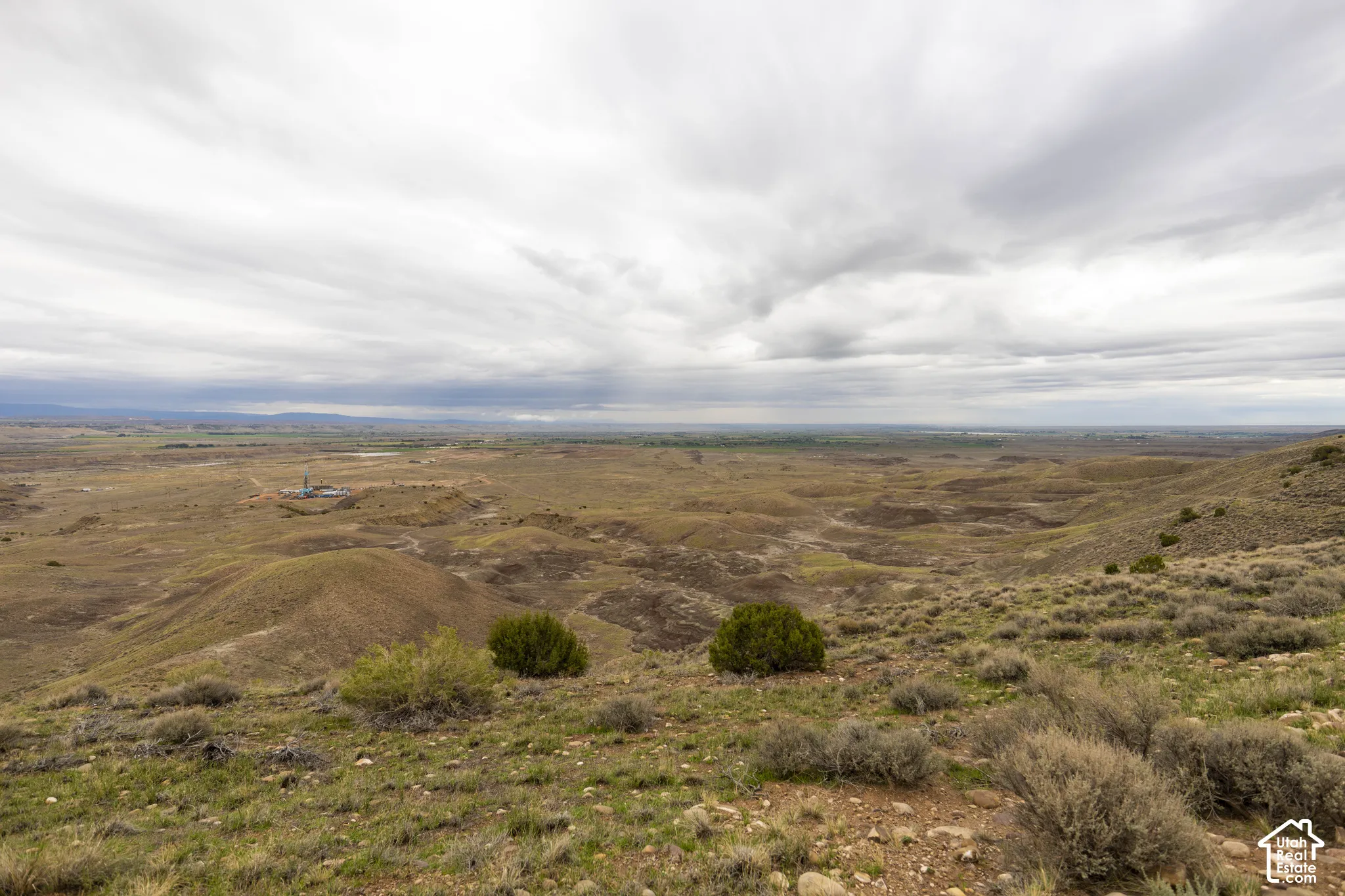 Expansive high-desert landscape featuring rolling terrain, native shrubs, and mountain silhouettes
