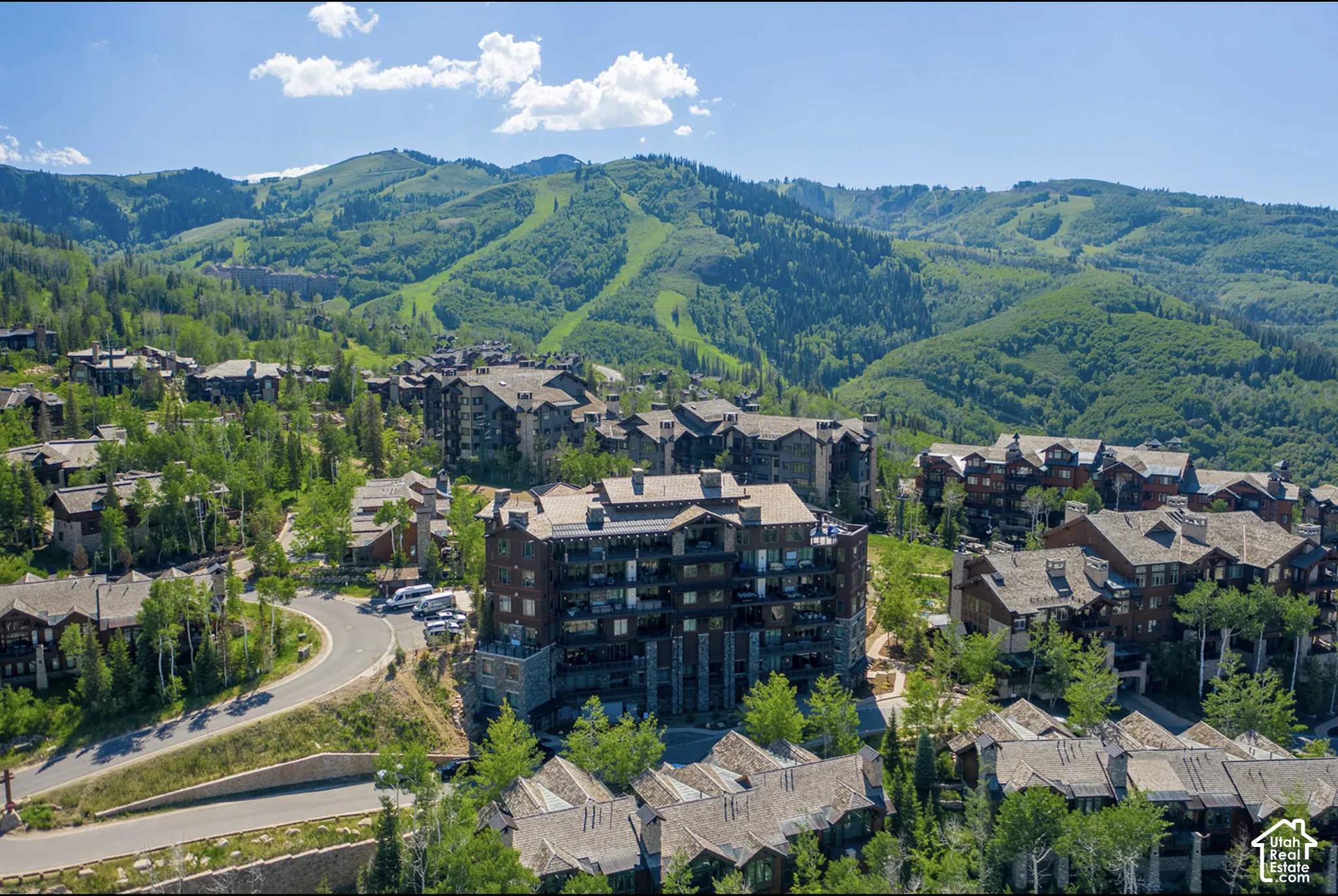 Multi-story mountain architecture featuring wood and stone exterior cladding, expansive private balconies, and a metal roof, situated against a backdrop of mountainous terrain