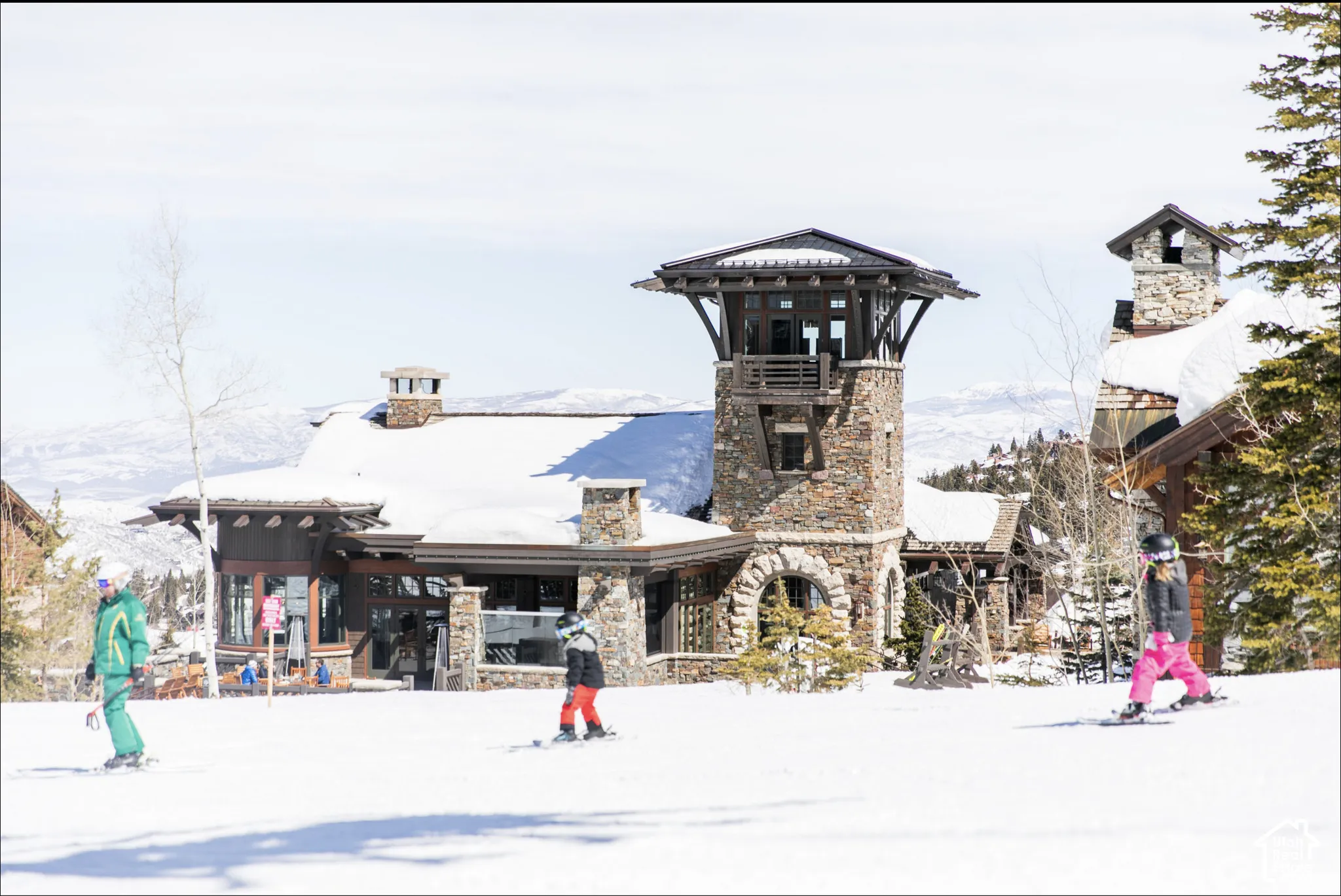 Stone and timber exterior architecture featuring a prominent central tower, arched masonry detailing, exposed beam accents, and exterior stone chimneys