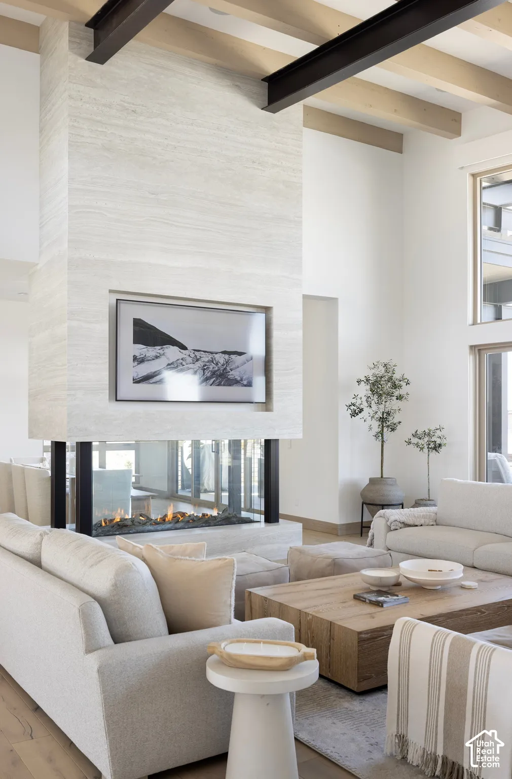 Floor-to-ceiling stone fireplace surround, double-sided glass hearth, exposed wood ceiling beams, steel structural support beams, and oversized windows