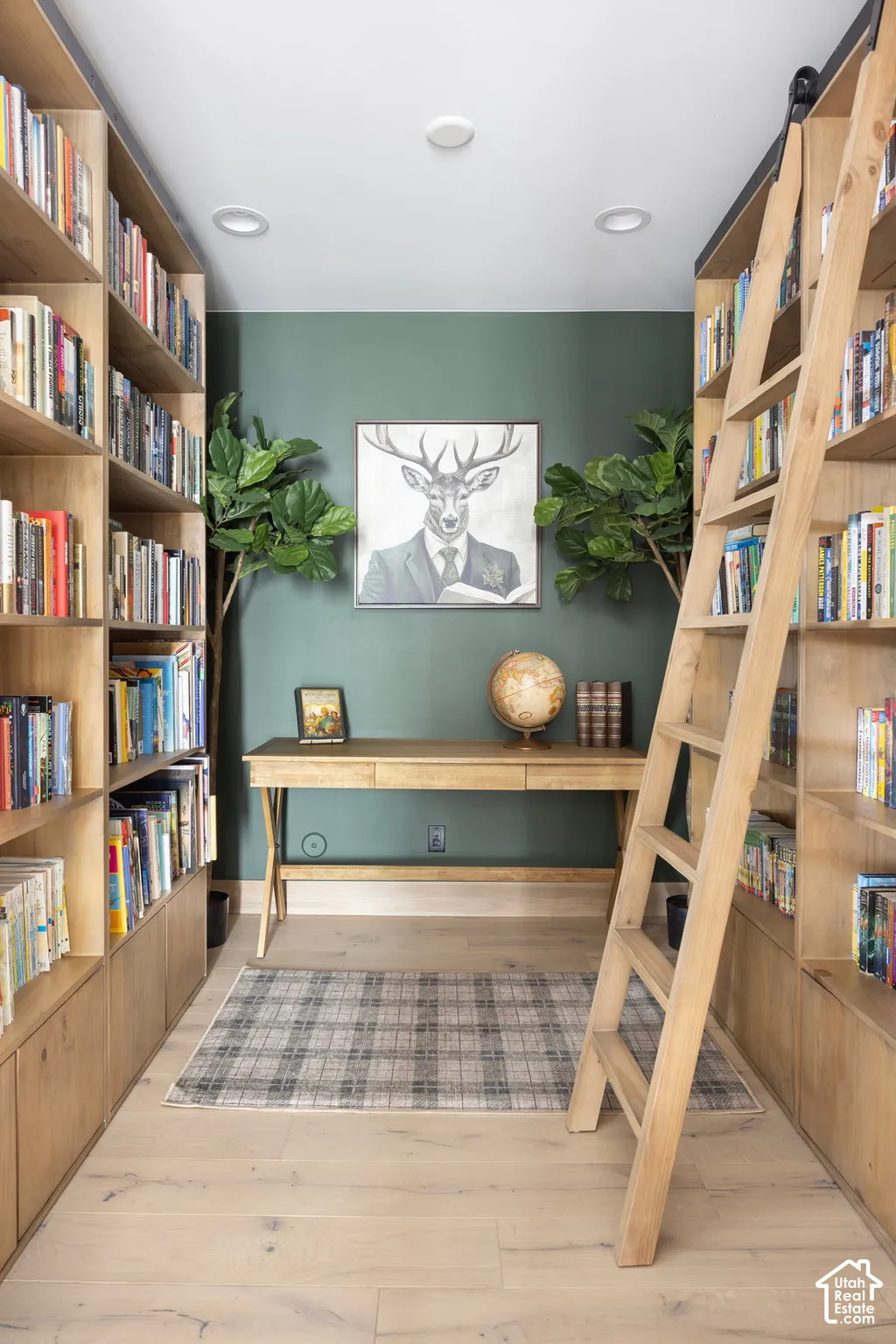 Floor-to-ceiling built-in wooden shelving, integrated rolling library ladder, recessed ceiling lighting, and light-tone wood-finish flooring