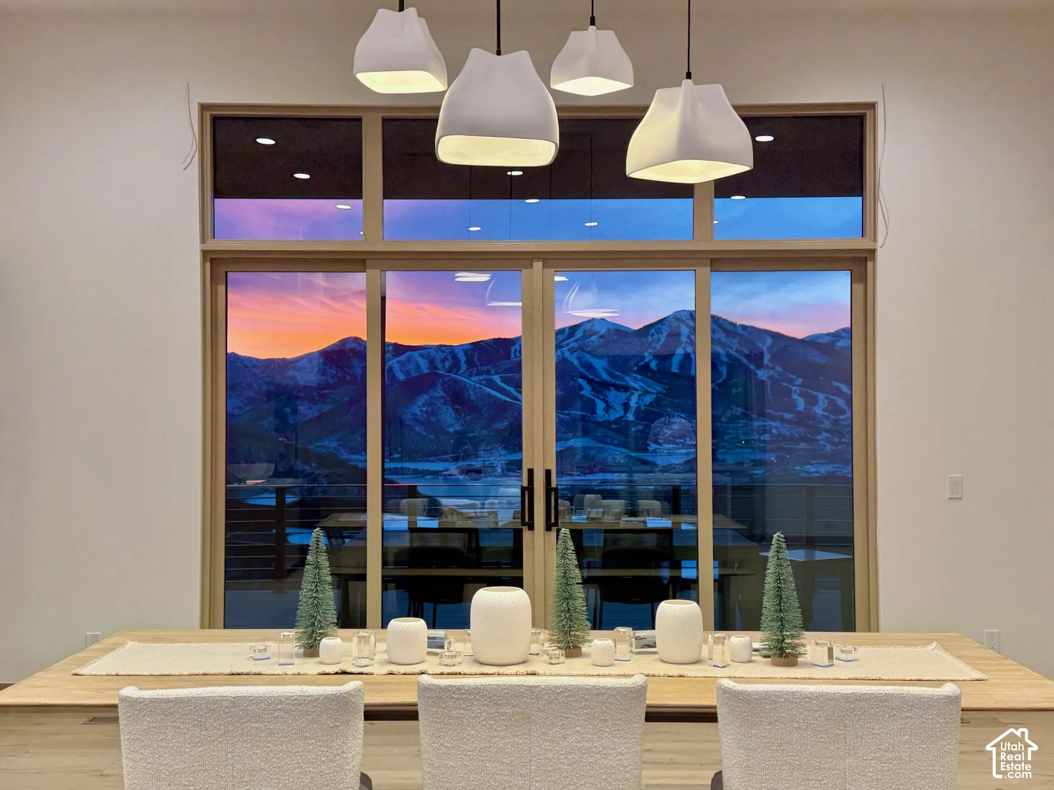 Expansive floor-to-ceiling glass panel windows with a mountain backdrop, sliding glass door, and modern multi-pendant lighting fixture