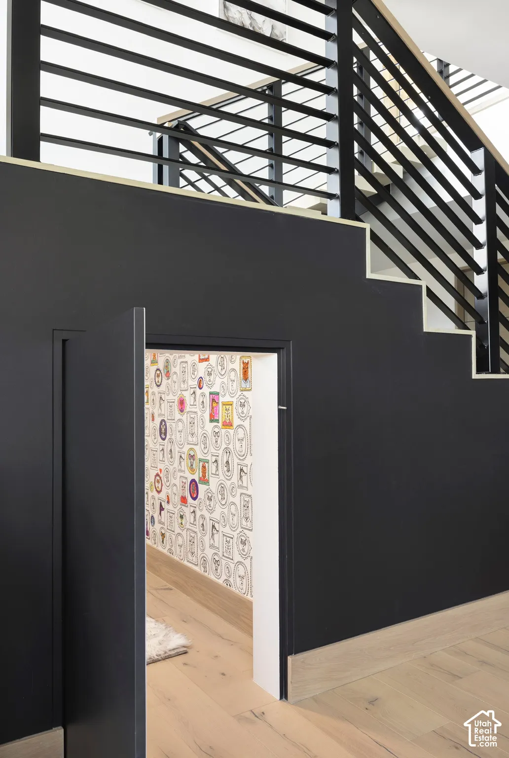 Staircase featuring a matte black solid panel wall, horizontal metal railing system, and light wood-finish flooring