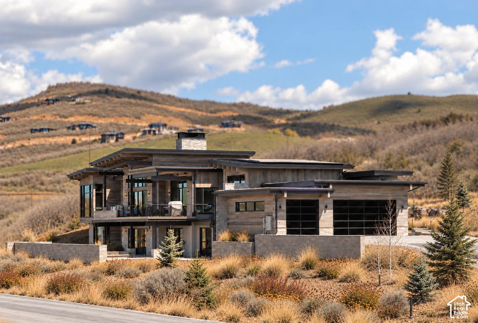Contemporary multi-level exterior featuring stone and wood-composite siding, expansive floor-to-ceiling windows, integrated stone chimney, and multi-car garage with glass-paneled doors