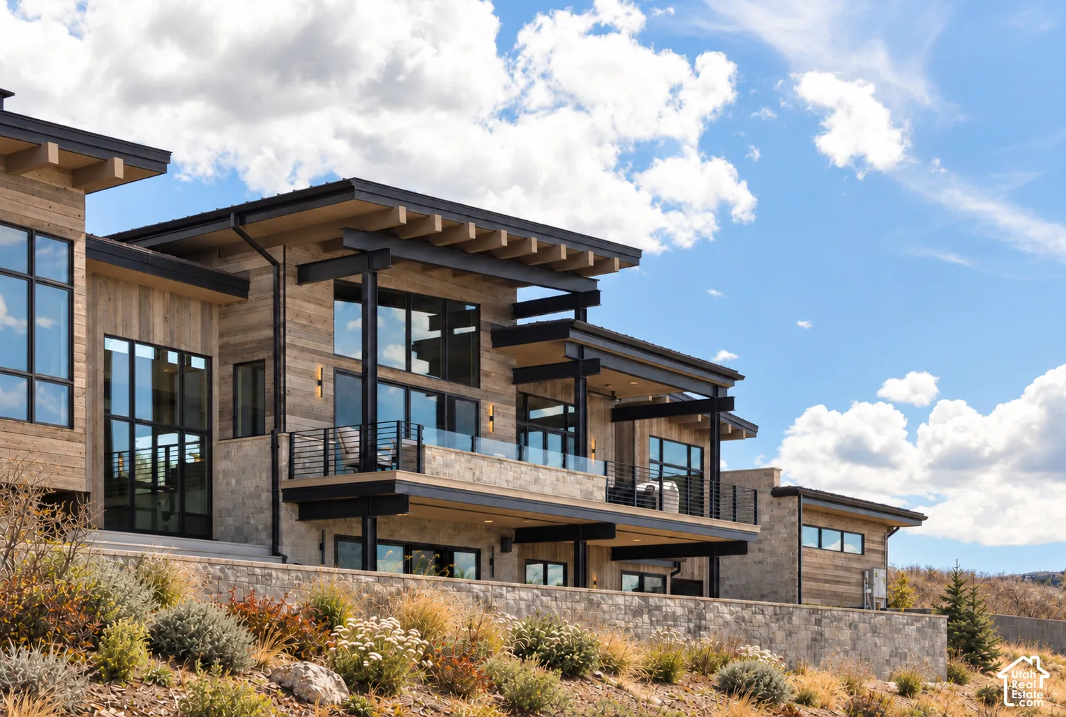 Contemporary exterior featuring vertical wood siding, stone masonry, expansive floor-to-ceiling windows, exposed structural timber beams, and multilevel balconies with glass railings