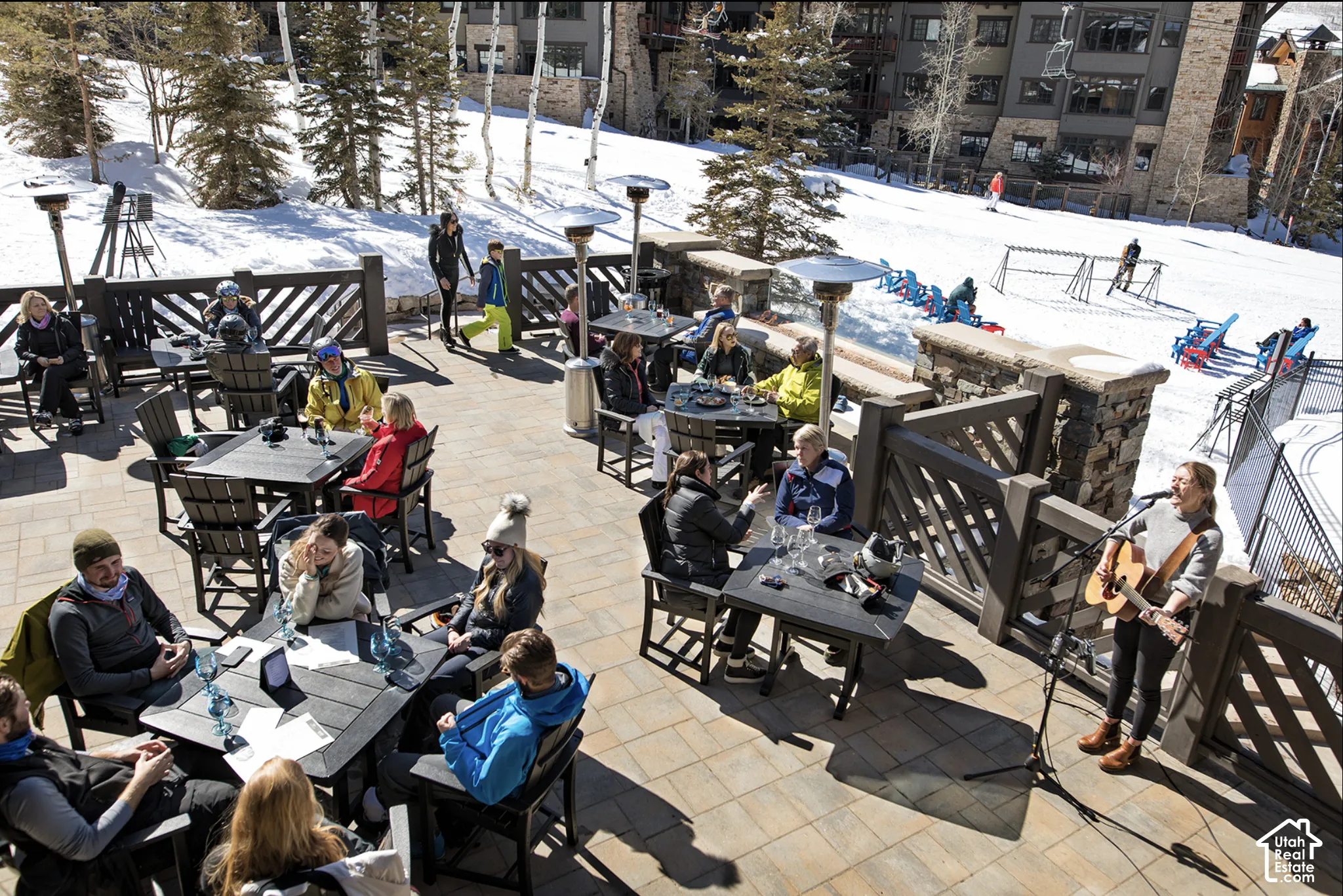 Expansive stone-paver terrace featuring built-in stone pillar accents, dark wood-finish railings, and integrated metal heating fixtures