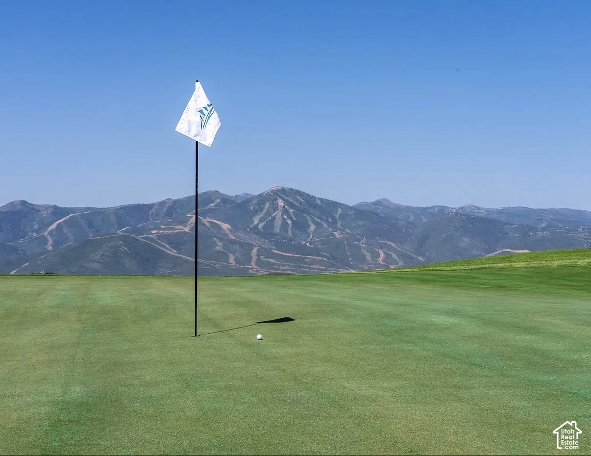 Manicured putting green featuring a pin flag and mountain backdrop