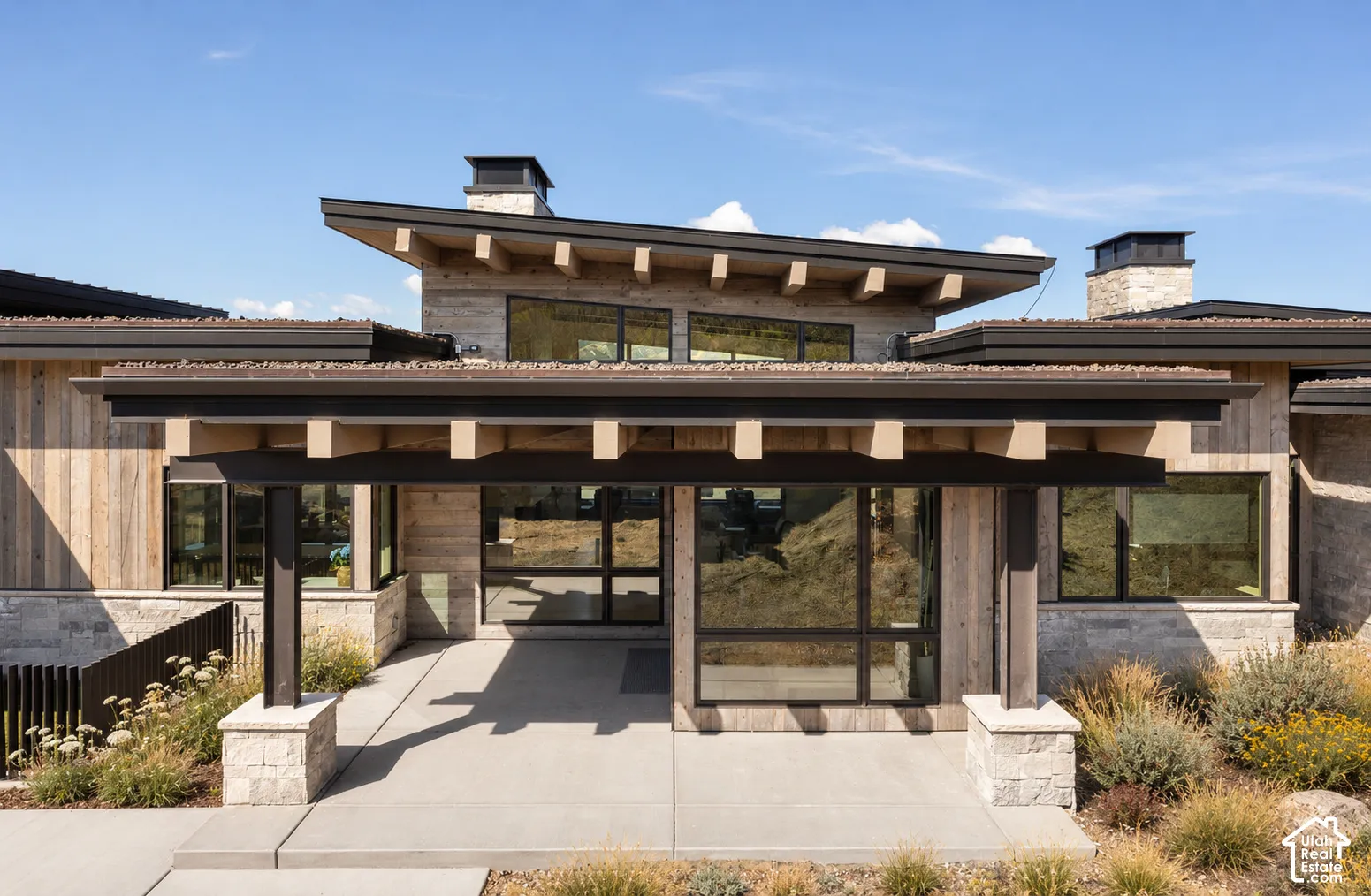 Contemporary architectural exterior featuring wood siding, stone masonry, a shed roofline with exposed rafter tails, and expansive multi-pane windows