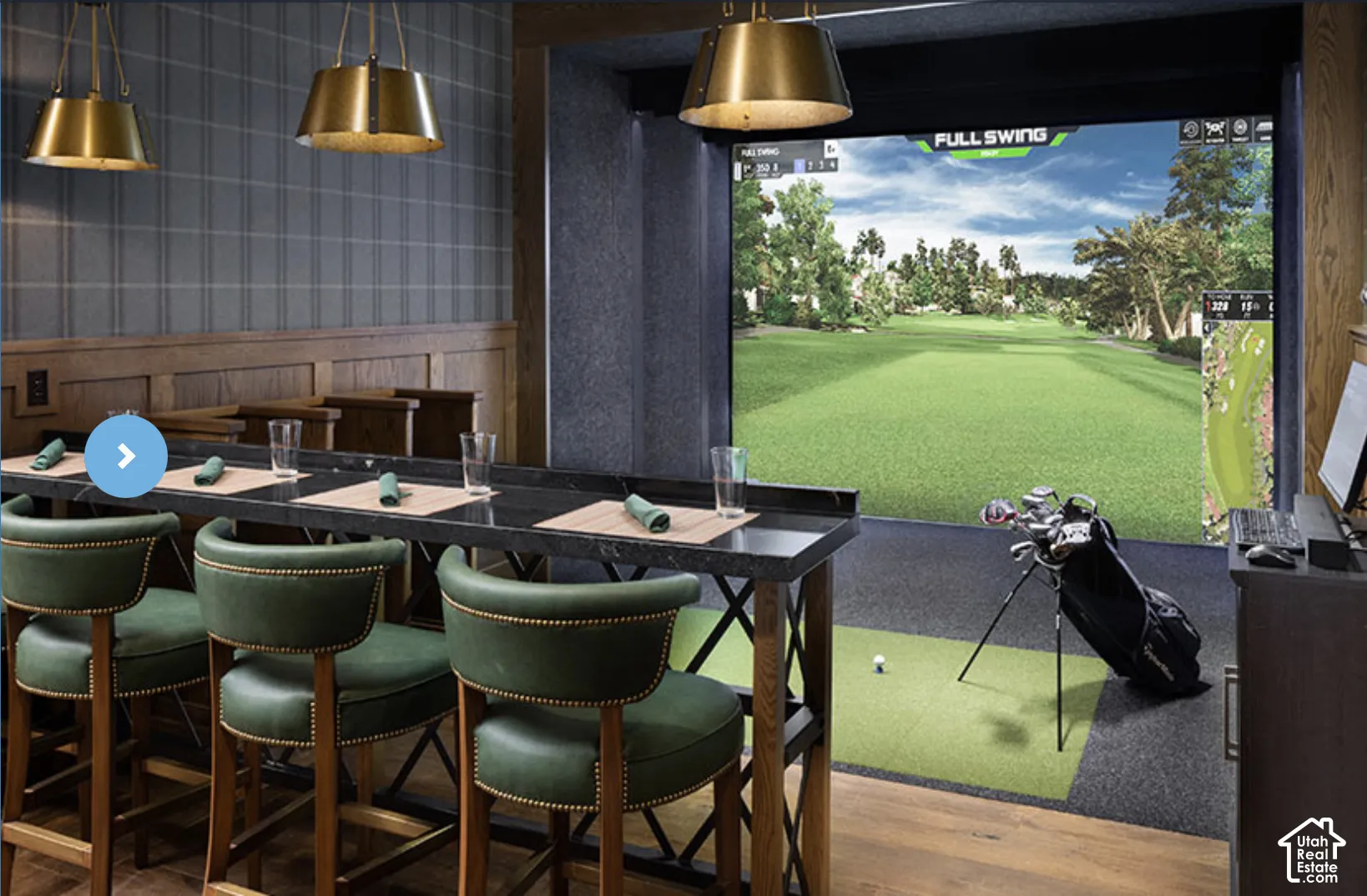 Golf simulator room featuring an integrated projection screen, high-top bar with dark stone countertop, wood wainscoting, and metallic pendant lighting