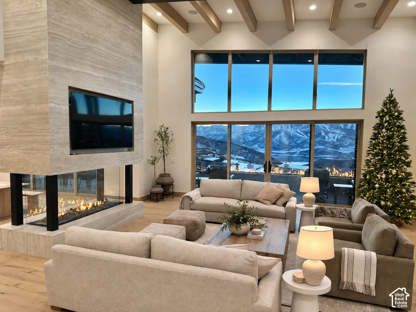 Floor-to-ceiling stone fireplace, soaring vaulted ceilings with exposed wood beams, expansive glass window wall, and wood-finish flooring